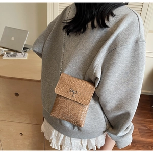 Detail of tan woven texture bag featuring a metal bow and long chain strap for women