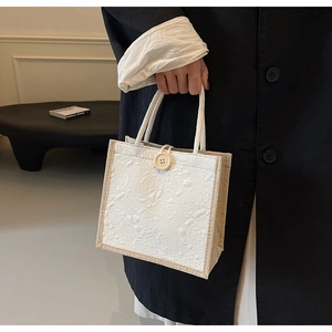 Detail of cream handbag featuring 3D rose relief and woven rope handle on linen sides
