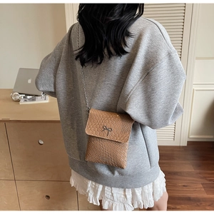 Detail of light brown woven texture shoulder bag with elegant black bow metal charm