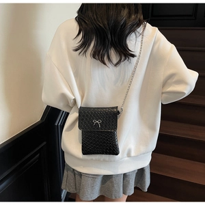 Detail of a black woven crossbody bag with a silver bow decoration and metallic chain