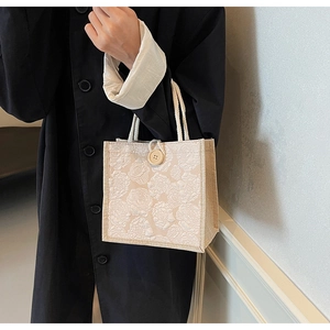 Detailed macro of floral relief texture and wooden button closure on small linen tote
