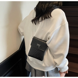 Detailed view of black woven texture shoulder bag with silver bow on white sweater