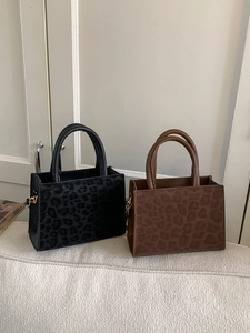 Fashionable leopard print tote bag in black and mocha brown on a cozy woven sofa