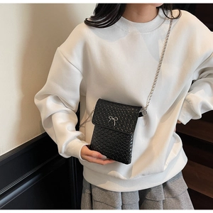 Close-up of black crossbody phone bag with woven texture, silver bow and chain strap