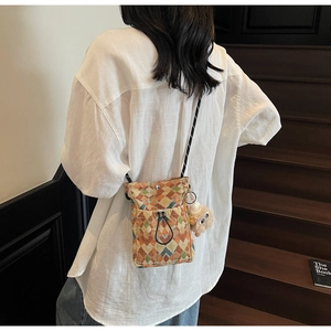 Detail of woven crossbody bag with geometric patterns and cute plush keychain accessory