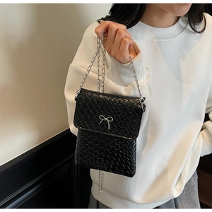 Close-up of black woven phone bag featuring silver bow detail and metallic chain strap