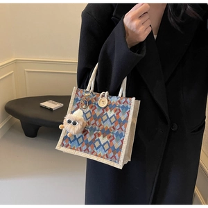 Detail of checkered linen tote bag featuring a white rope handle and a cute plush monster charm