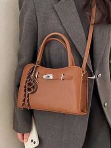 Brown lychee leather shoulder bag with pretzel charm and woven rope detail on grey suit