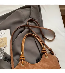 Detail of a brown leather bucket bag with adjustable straps and knot decoration on gray fabric