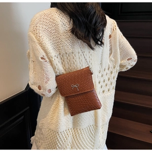 Close-up of caramel woven crossbody bag with silver bow accent on knit fabric