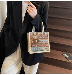 Ethnic woven tote bag with white rope handles and a cute brown plush monster charm
