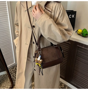 Detail of brown suede Boston bag with teddy bear charm and adjustable strap worn on coat