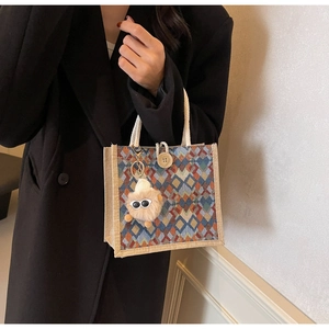 Detail view of woven tote with colorful argyle pattern, wooden button and plush eye charm