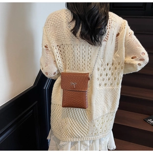 Detail of a brown woven leather crossbody bag with a silver metal bow on a chain strap