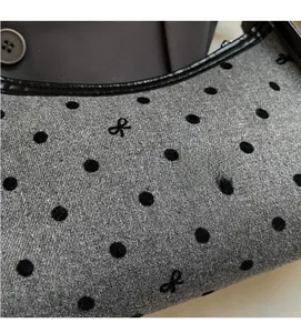 Close-up of gray wool fabric featuring black velvet polka dots and bow embroidery detail