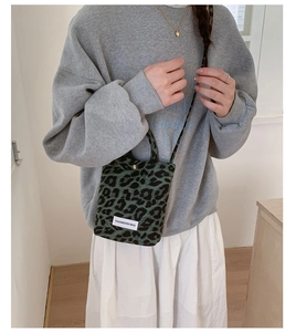 Detail shot of a small green leopard print tote bag with a white brand label and crossbody strap