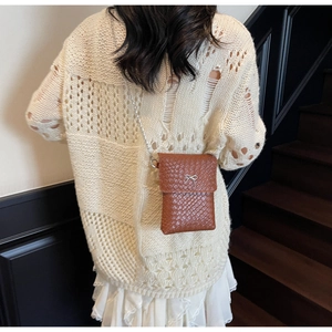 Detail of a brown woven crossbody bag with a silver bow clasp on a metal chain strap