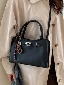 Classic black leather crossbody bag with silver buckle and retro charms on beige trench