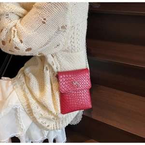 Detail of red woven leather crossbody bag with a silver metal bow buckle on a model