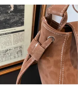 Close-up of brown suede bucket bag featuring white contrast stitching and drawstring detail