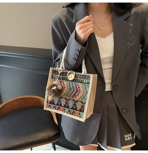 Detail of woven tote bag with ethnic pattern and lion plush pendant on grey blazer