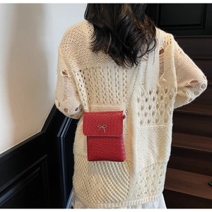 Detail of red leather woven mini crossbody bag with silver bow on cream knit sweater