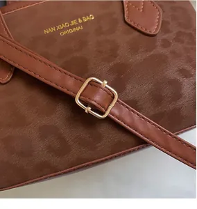 Detail of brown faux suede tote with leather strap and golden adjustable metal buckle