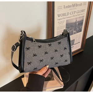 Detail of grey wool underarm bag with black bow patterns and leather shoulder strap