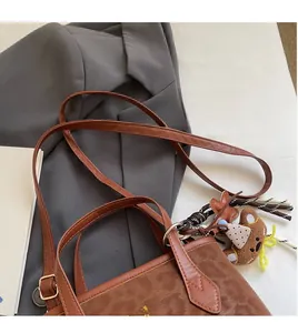 Detail of a brown leather tote with leopard texture, adjustable strap and bear charm