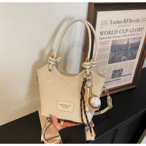 Detail of beige leather bucket bag with baseball charm and decorative knot on strap