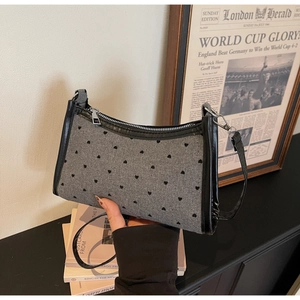 Detail of grey tweed baguette bag with black heart patterns and adjustable shoulder strap
