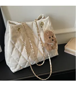 Detail of white quilted tote bag with golden chain strap and brown puppy plush pendant