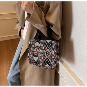 Detail of ethnic tote bag showing geometric embroidery and black woven handles on beige coat