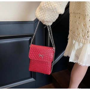 Detail of red woven leather shoulder bag with silver bow accent and metal chain strap