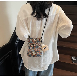 Sac bandoulière pour téléphone avec motif tissé coloré et breloque peluche sur escalier