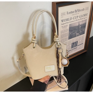 Detail of cream bucket bag with wavy rim, knot handle, and baseball themed keychain charm