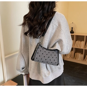 Polka dot underarm bag with a bow detail and black trim shown in a cozy indoor setting
