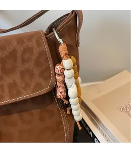 Detail of beaded bag charm with vintage patterns hanging on a brown leather bucket bag