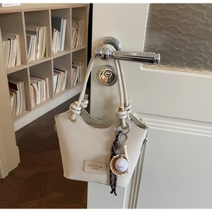 Detail of cream bucket bag featuring NAN XIAO JIE logo and baseball theme charm