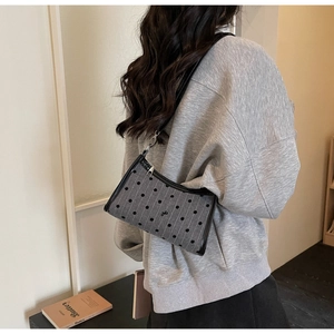 Detailed side view of grey polka dot underarm bag with black bow and stripe pattern