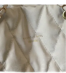 Detail of quilted diamond pattern and gold brand logo on beige leather tote bag