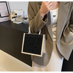 Detail of a black floral embossed tote bag with beige canvas trim held by a model