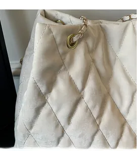Macro detail of quilted cream tote bag showing soft fabric texture and chain strap
