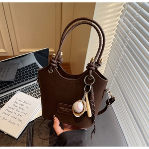Detail of a brown bucket bag with unique knotted circular handles and a baseball charm