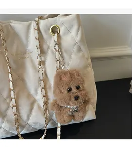 Detail of white quilted tote bag featuring gold chain strap and cute plush dog charm