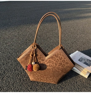Close-up of leopard print tote bag with plush pom-poms and leather straps detail