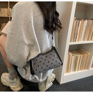 Polka dot underarm bag with black leather trim and bow detail shown on shoulder