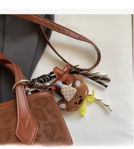 Detail of brown leather tote bag featuring a cute plush bear charm and woven tassel