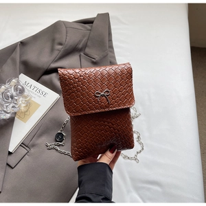 Detailed view of brown woven texture handbag with metal bow buckle and silver chain strap