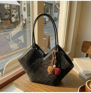 Close-up of leopard print tote bag with colorful pom-pom charm on a wooden table